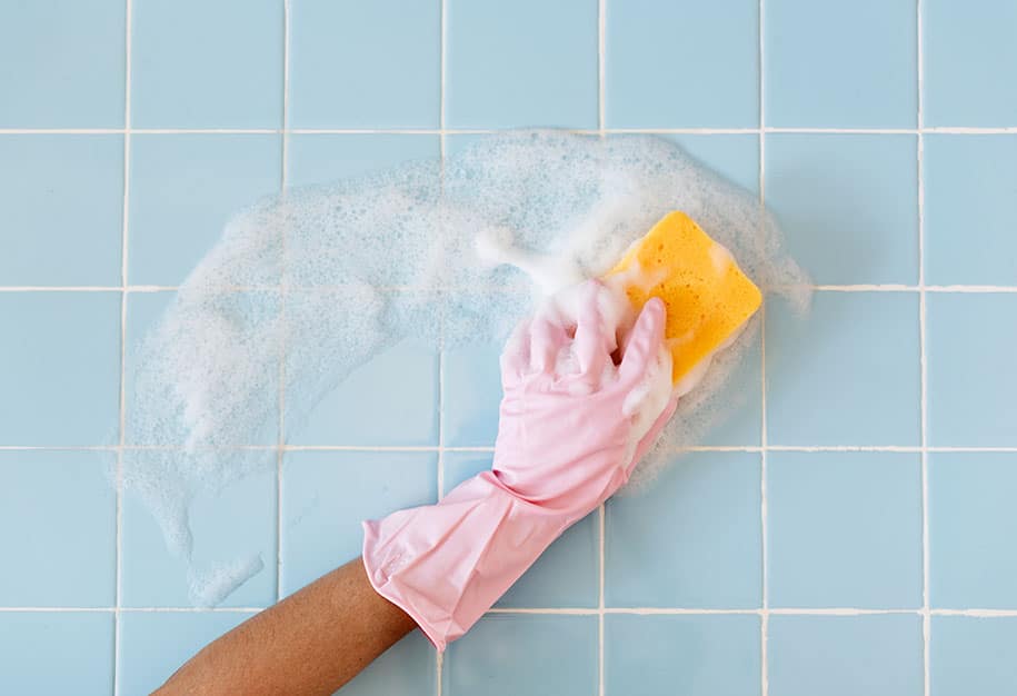 Individual with gloves cleaning painted tile walls with sponge and soap