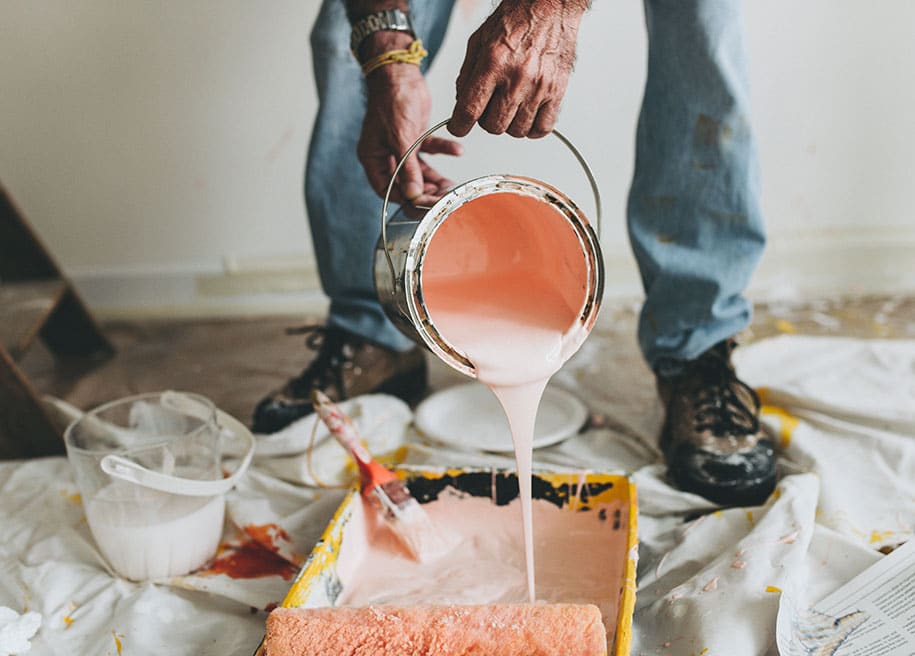 Man pouring pink paint onto painting equipment on the floor covered with a cloth